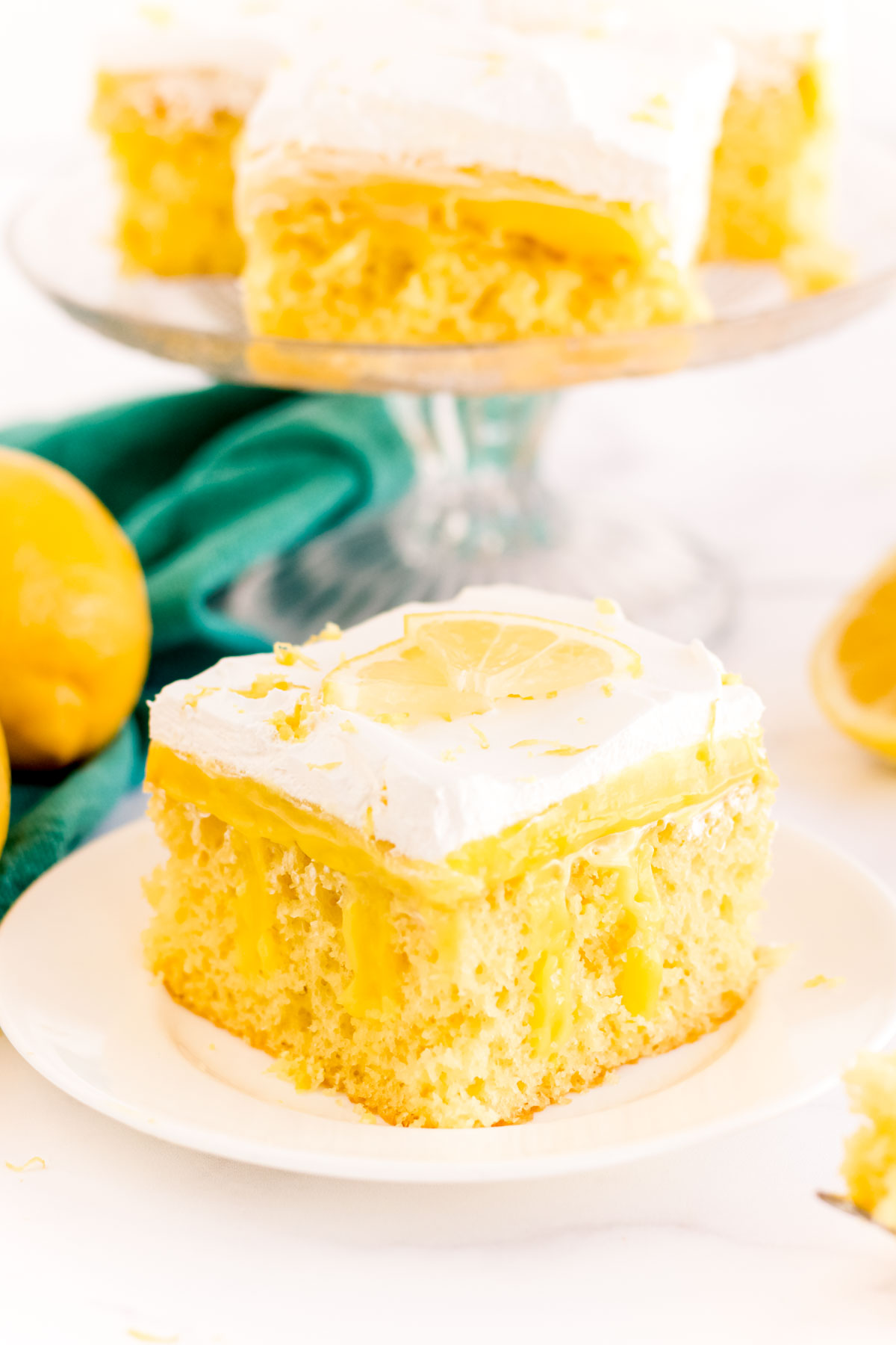 Close up photo of a slice of lemon poke cake on a white plate.