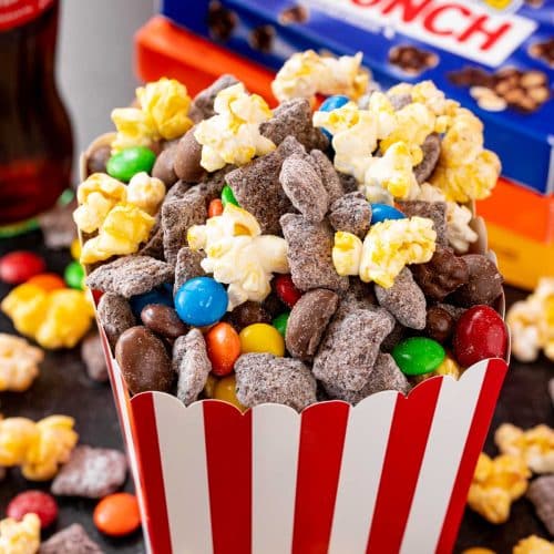 Movie night popcorn snack mix in a red and white paper box with boxes of candy in the background.