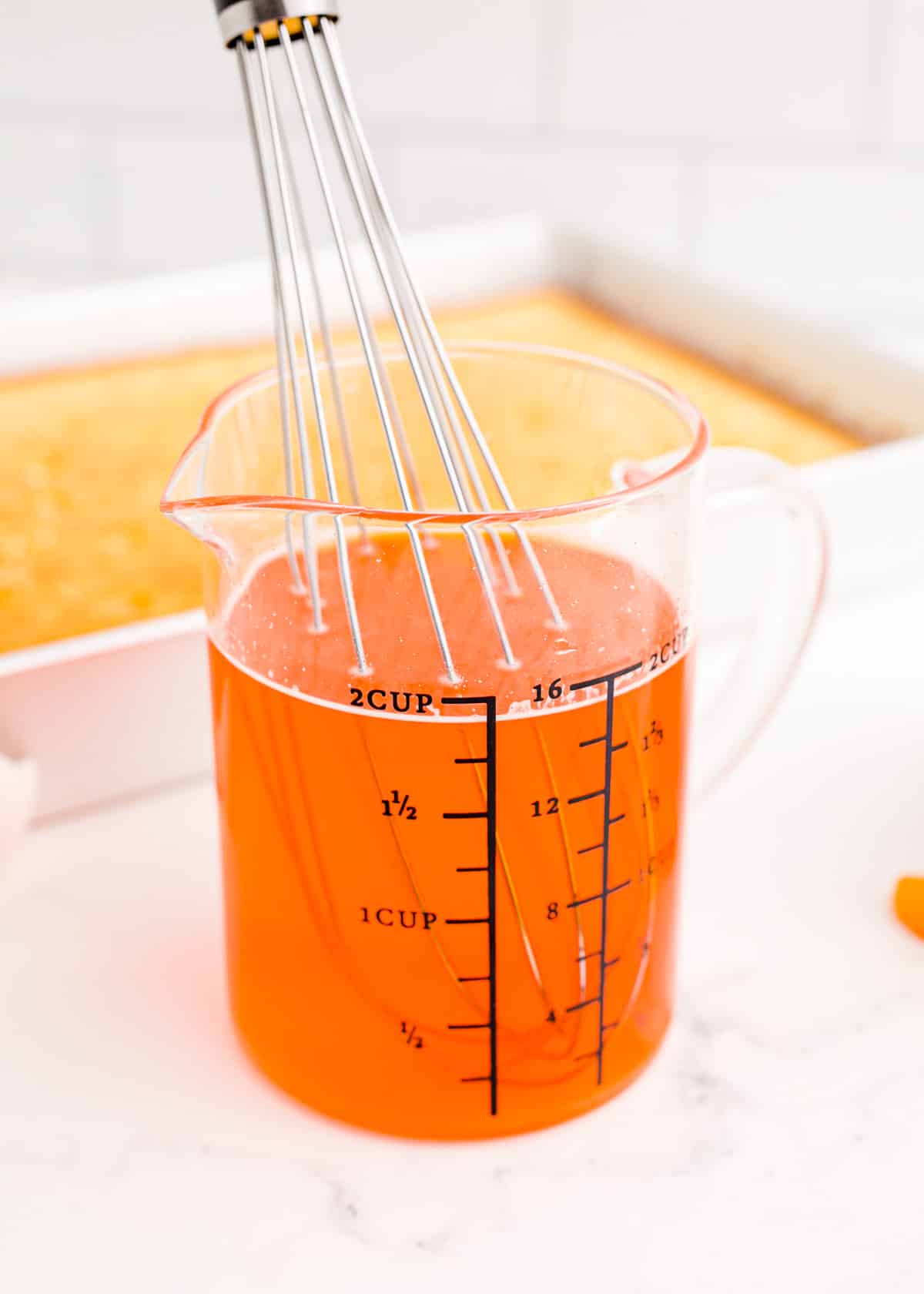 Orange jello being whisked in a measuring cup.