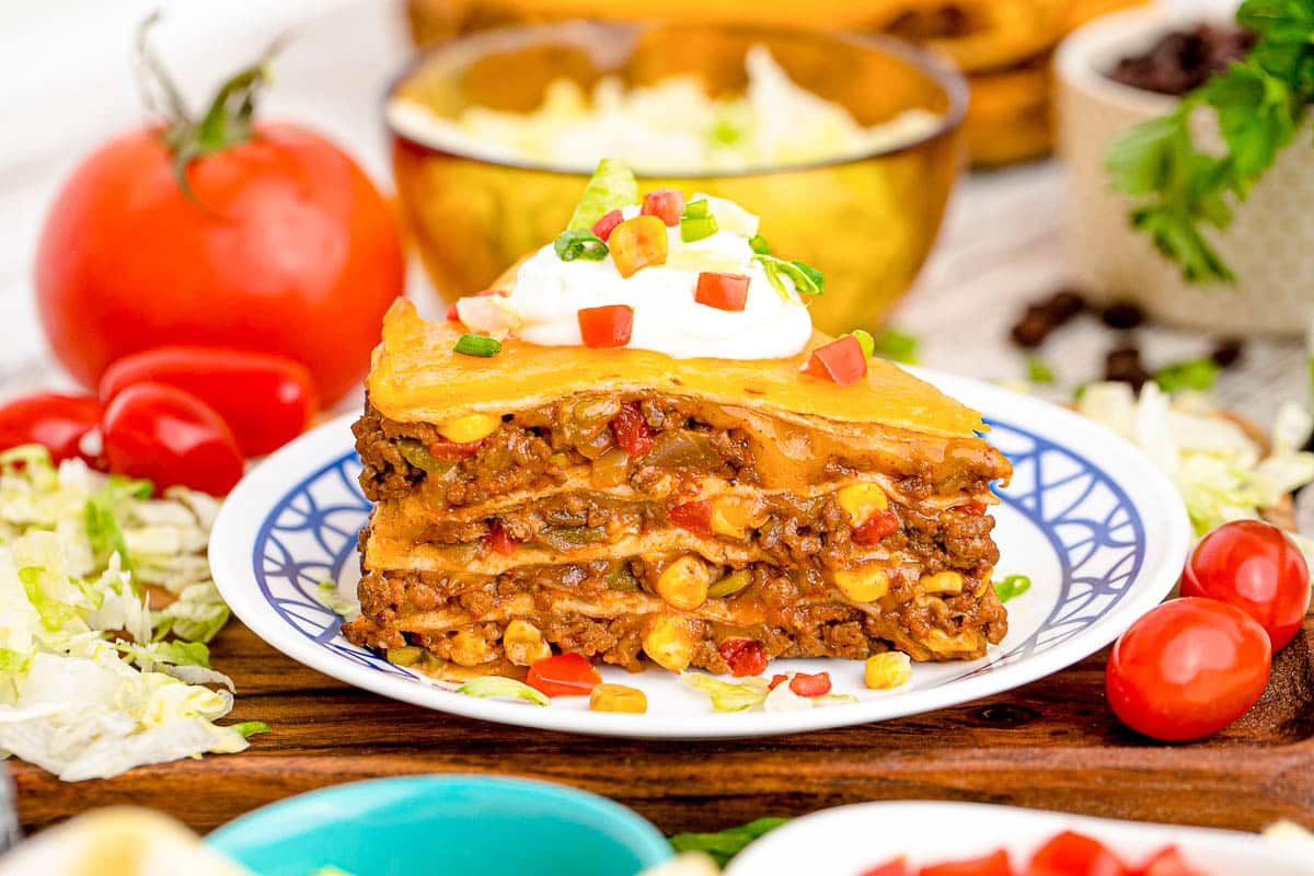 Close up photo of a slice of layered taco pie on a white plate with blue trim.