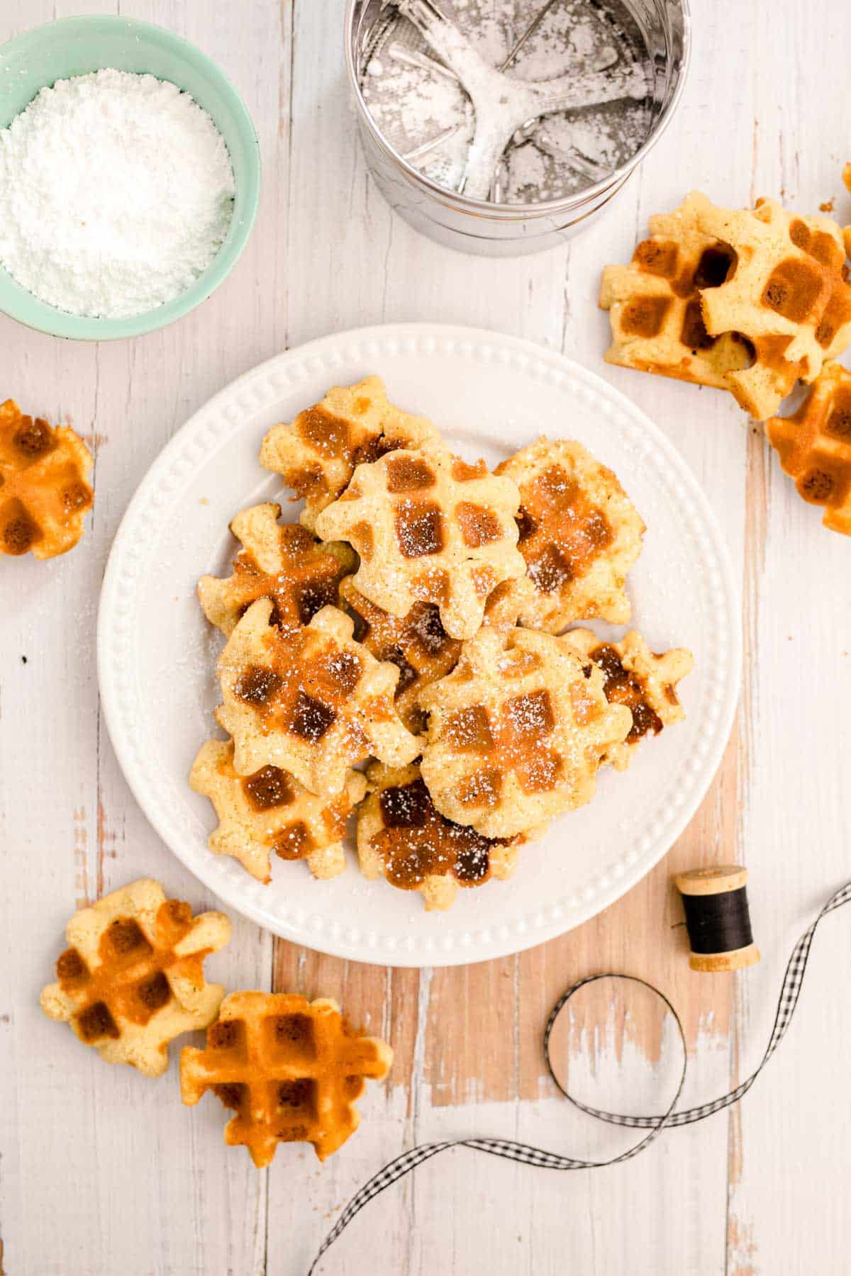 Overhead photo of waffle cookies on a white plate on a white wooden table.