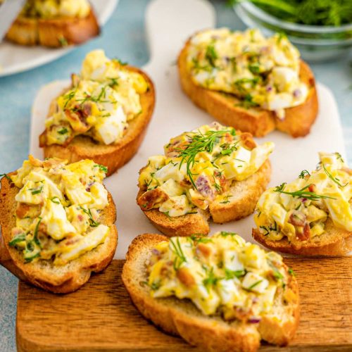 Bacon egg salad crostinis on a serving board.