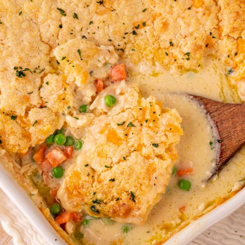 Overhead photo of a baking dish filled with chicken cobbler, a spoon is taking a scoop out of it.