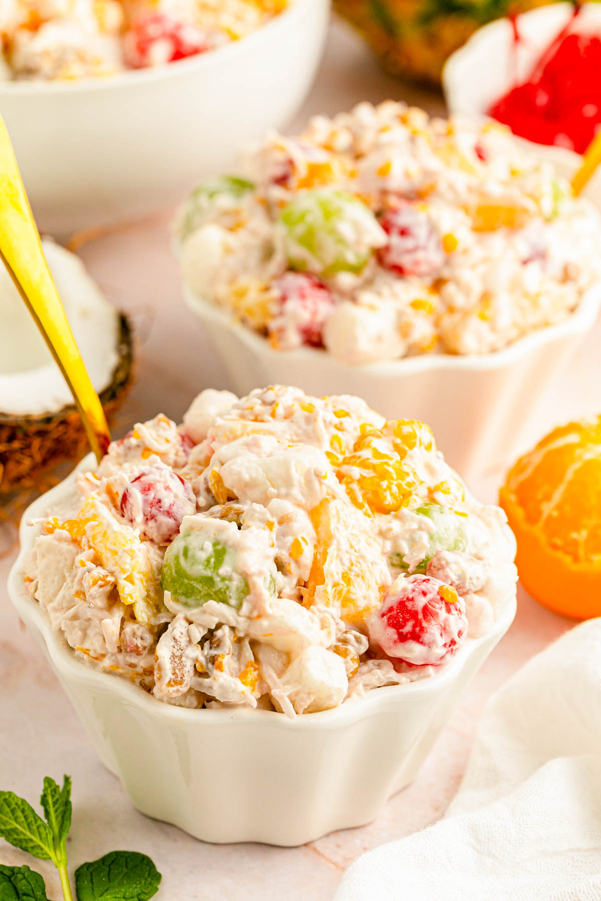 A small white bowl of ambrosia salad with more bowls around it.