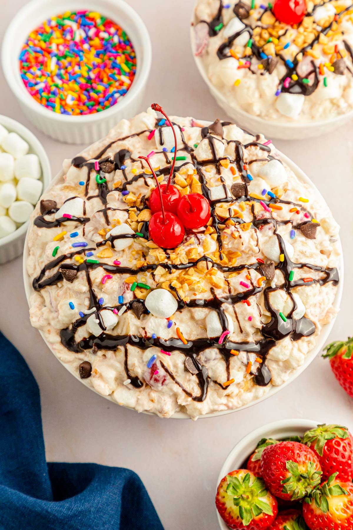 A big bowl of banana split fluff salad on a counter with other bowls of toppings and fruit around it.