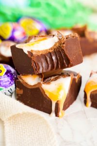 A stack of two pieces of chocolate cadbury fudge made with creme eggs, the top one is missing a bite.