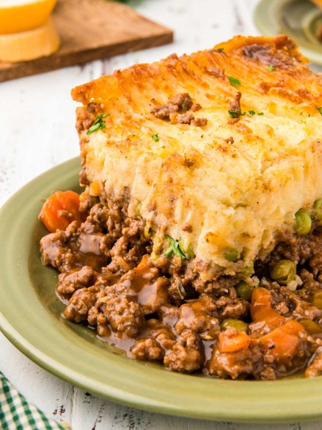A green plate with a large slice of cottage pie (shepherd's pie) on it.