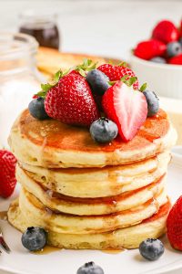 Homemade pancakes topped with berries on a white plate.