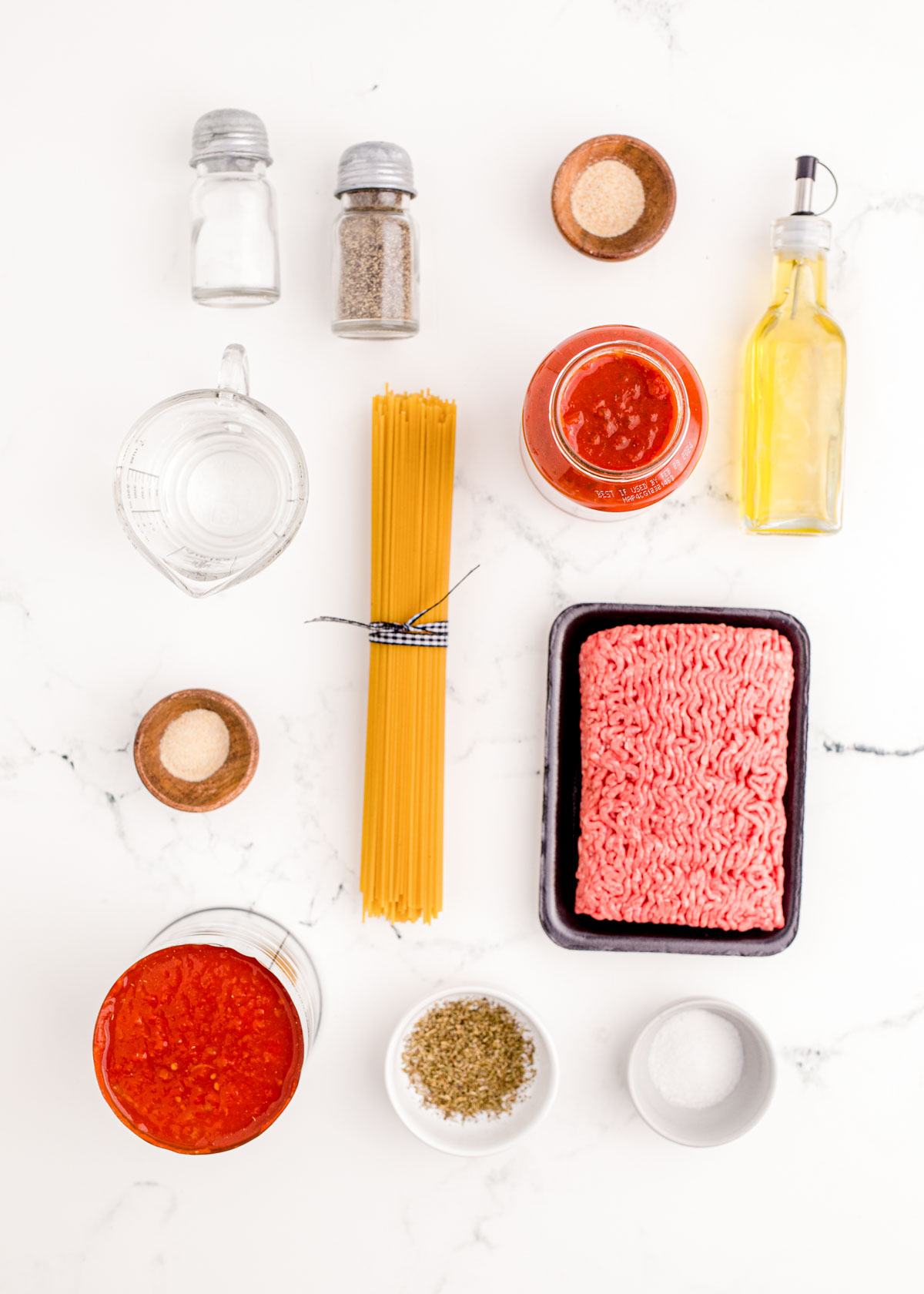 Ingredients to make spaghetti with meat sauce on a white table.