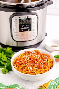 A white bowl filled with spaghetti and sauce in front of an instant pot.