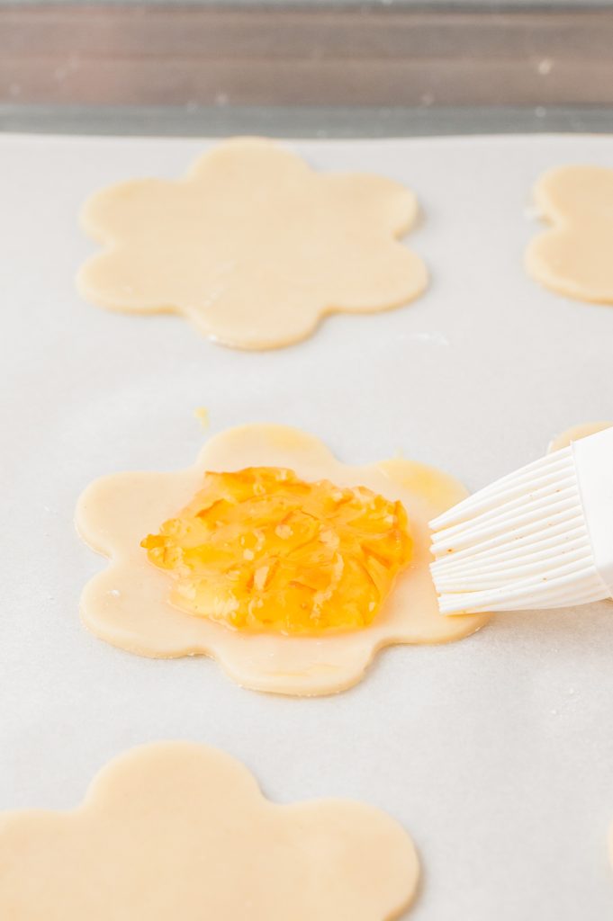 A flower shaped pie crust cookie being brushed with egg wash.