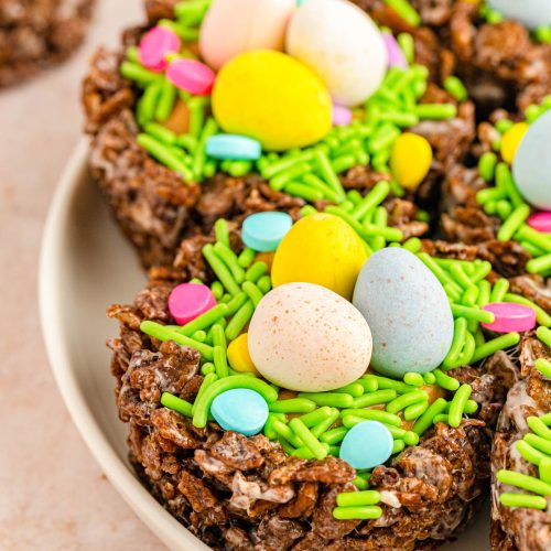 Close up of a plate filled with cocoa pebbles treats shaped like nests with chocolate eggs and colorful sprinkles for Easter or spring.