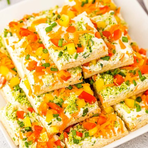 A white serving platter filled with veggie pizza squares for serving.