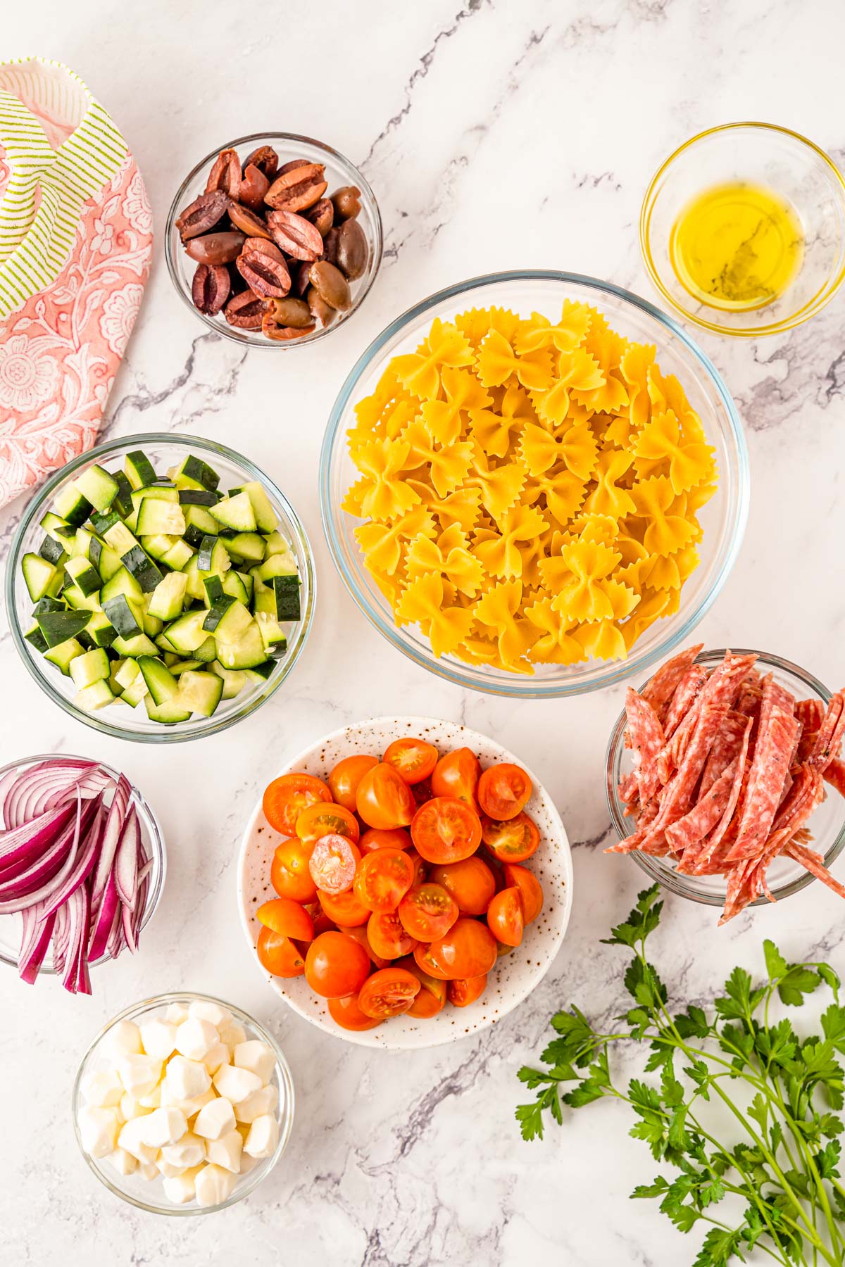 Overhead photo of ingredients to make Italian pasta salad on a marble counter.
