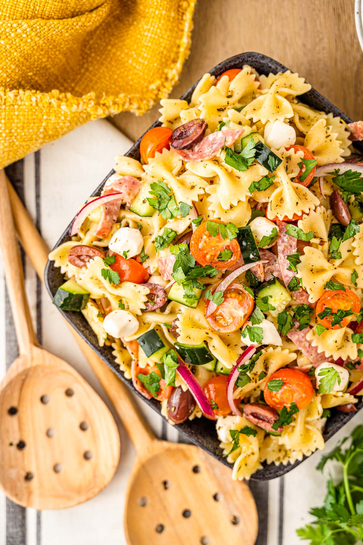 Overhead photo of Italian Pasta Salad in a black bowl on a table with wooden salad spoons.