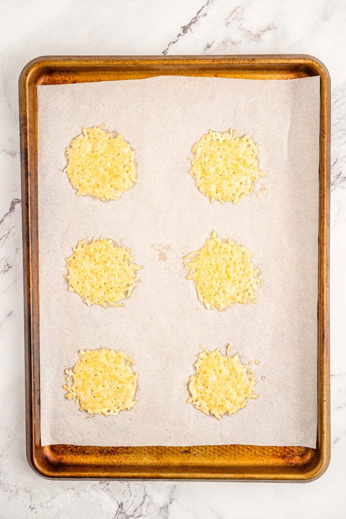 Parmesan cheese melted into circles on a piece of parchment paper on a baking sheet.
