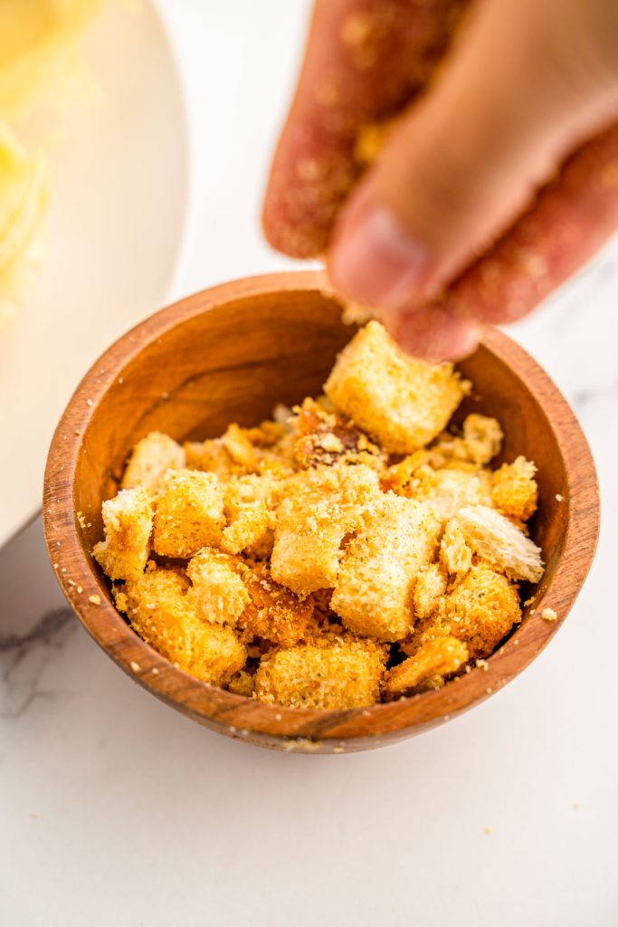 A woman's hand breaking up croutons in a wooden bowl.