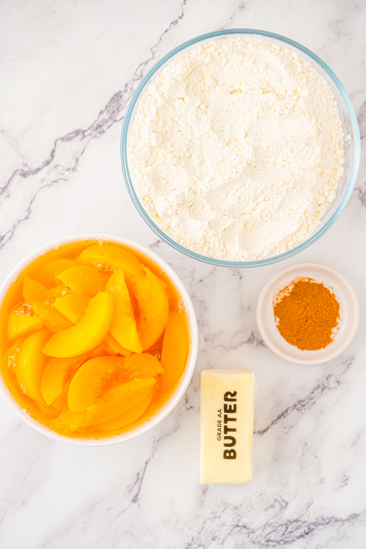 Ingredients to make peach dump cake on a marble counter.