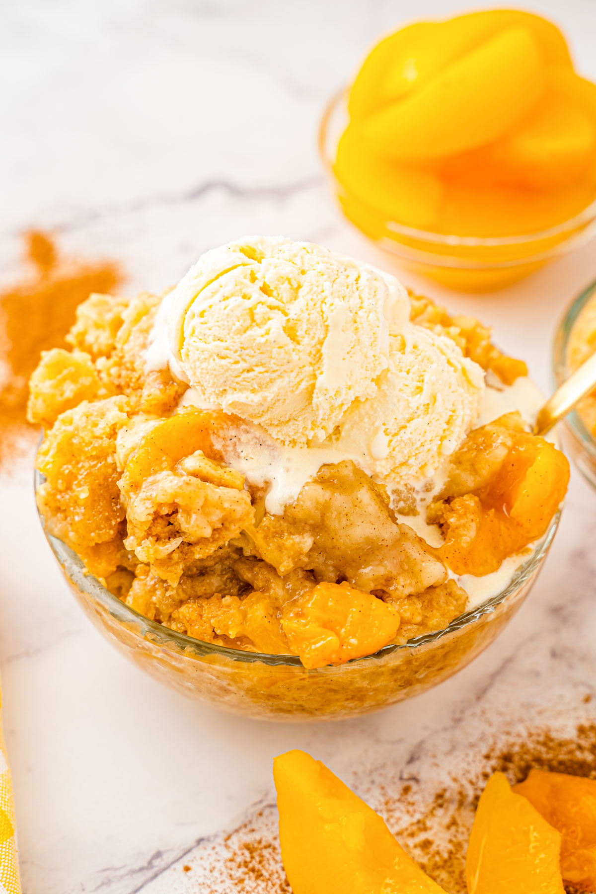 Peach dump cake in a glass bowl topped with ice cream. 