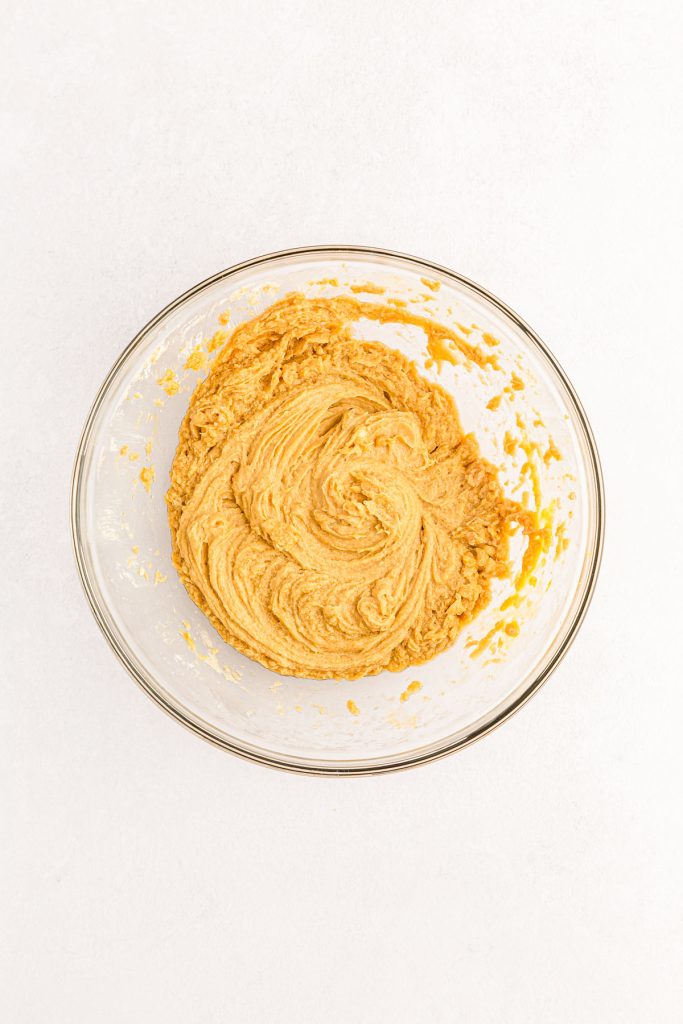Peanut butter, butter, and sugars creamed together in a glass mixing bowl.