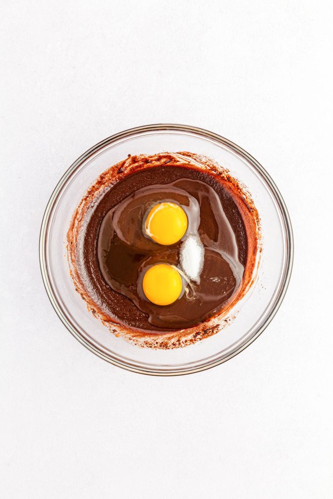 Two eggs added to a bowl to make brownie batter.