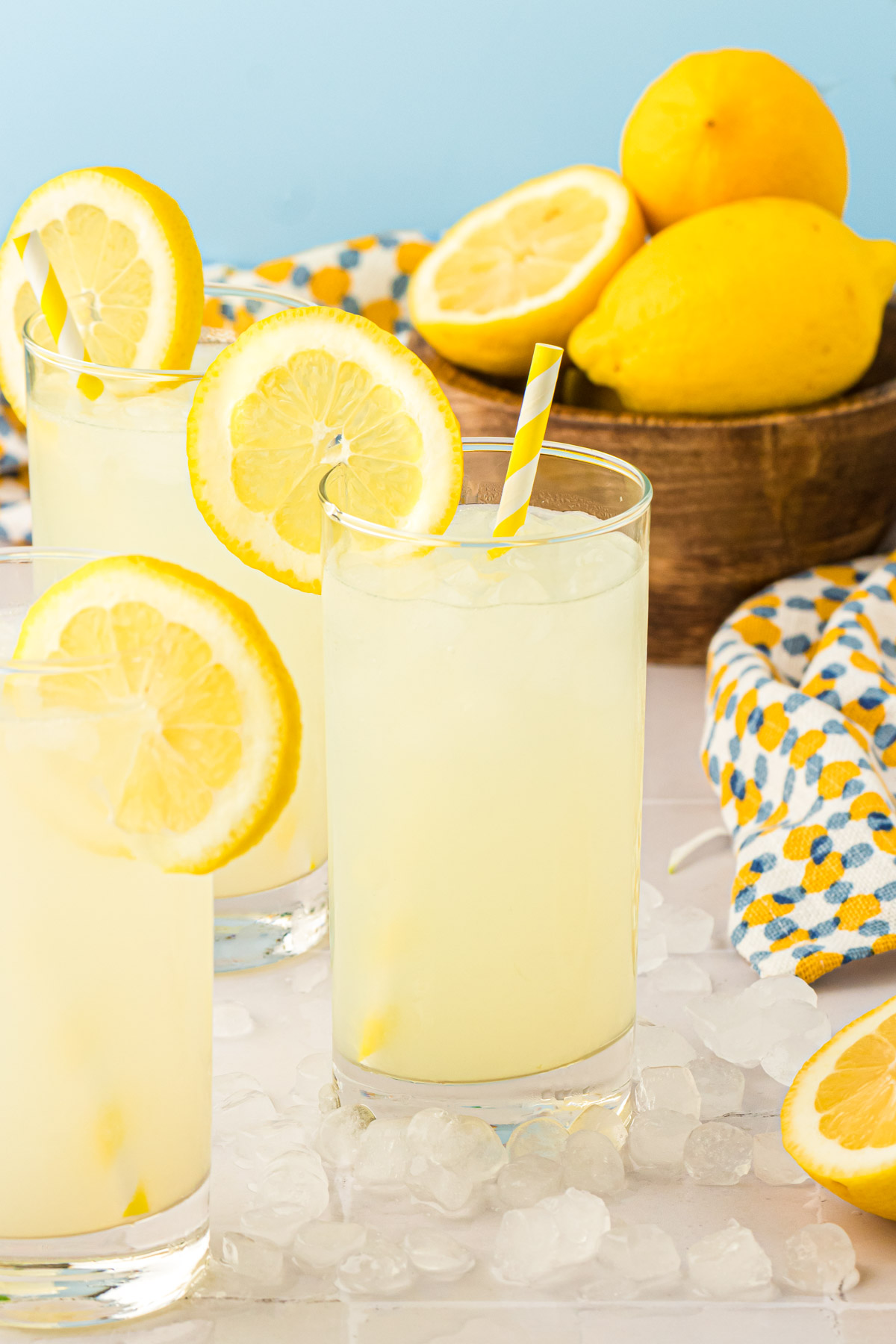 Glasses of lemonade on a gray table with ice around them.
