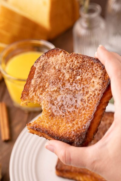 A woman's hand holding a piece of fried cinnamon sugar toast.
