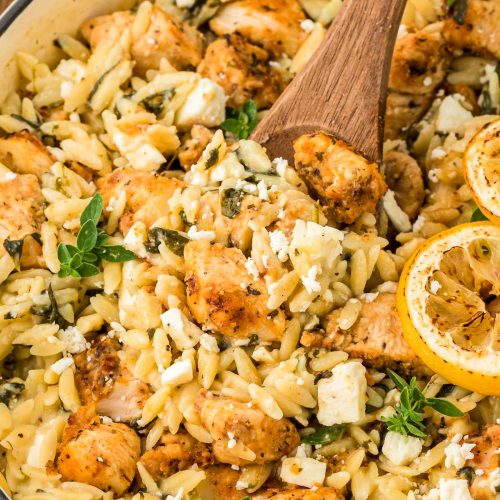 A wooden spoon in a skillet with lemon chicken orzo.