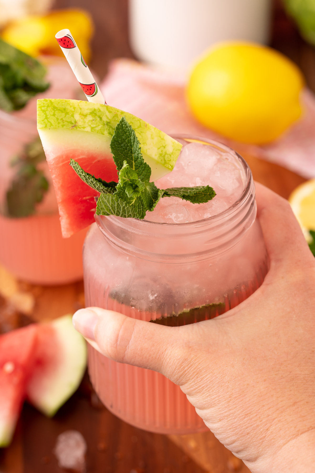 A woman's hand holding a mason jar filled with watermelon mint lemonade.
