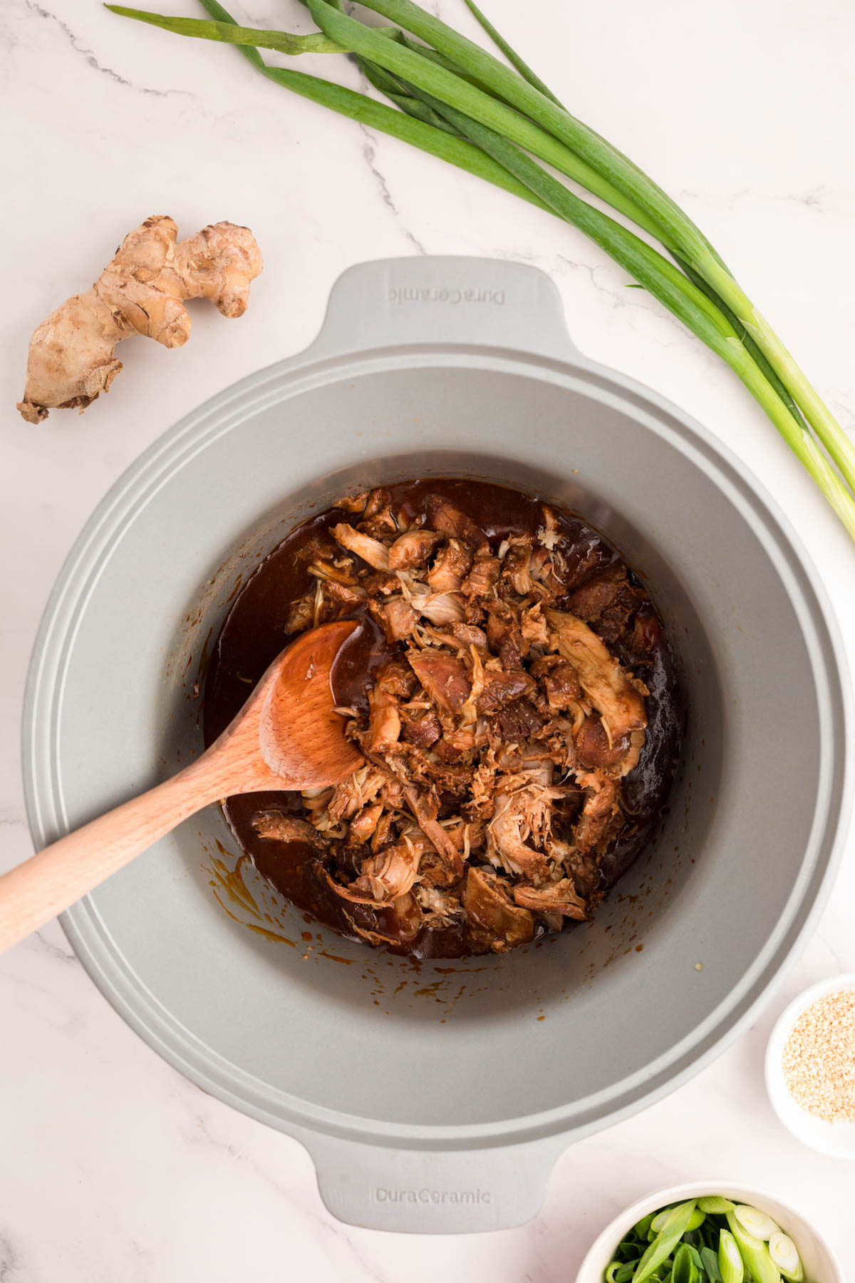 A wooden spoon stirring shredded chicken into honey garlic sauce in a crockpot.