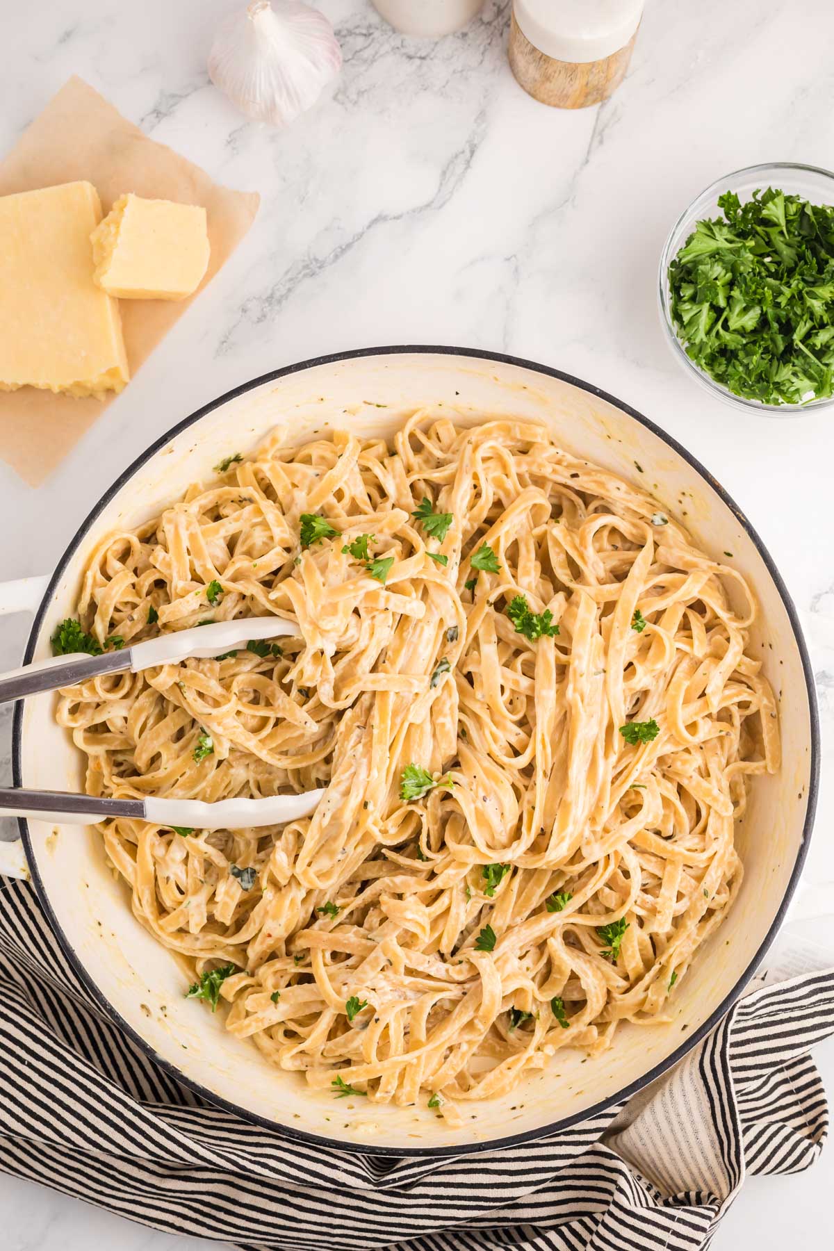 fettuccine alfredo in a skillet with tongs