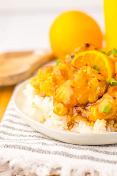 orange chicken on top of rice on top of a plate.